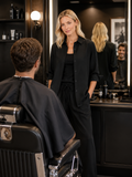 Female stylist wearing a relaxed black boyfriend shirt and wide leg pants while consulting with a client in a modern salon environment.