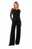 Model wearing the black mesh sleeve layering top under a tailored black vest and wide-leg trousers, demonstrating the sheer mesh sleeves and streamlined silhouette